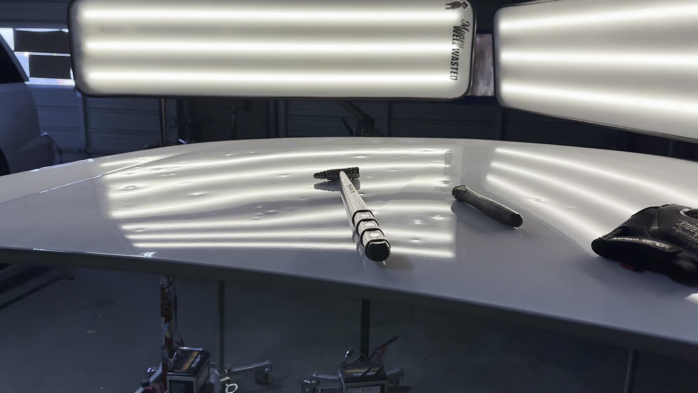 Hail-dented white hood under PDR inspection lights